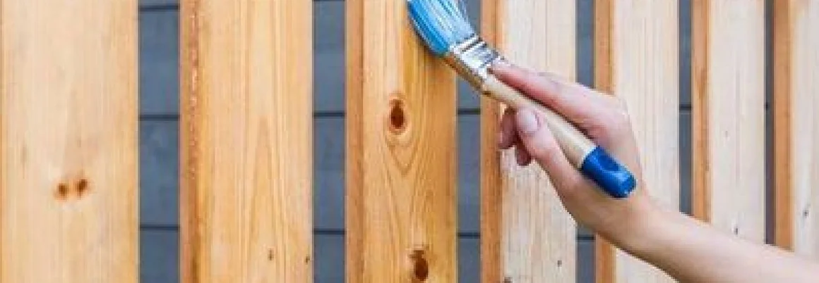 Person streicht Holzzaun mit Pinsel